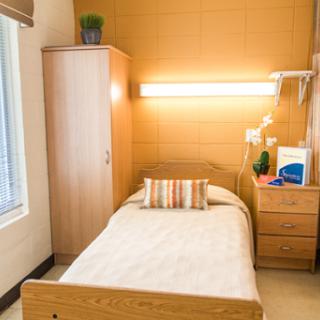 A cozy, minimalist hospital room featuring a single bed and wooden furniture.