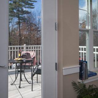 A cozy outdoor patio with a table and chairs, seen through an open door, with views of the surrounding trees.