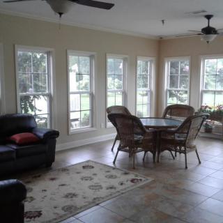 A bright sunroom featuring large windows, a seating area with a table and chairs, and a cozy sofa.