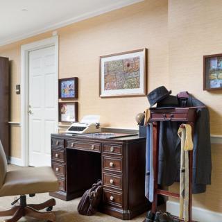 A traditional office setup with a wooden desk, typewriter, and clothing rack, complemented by framed artwork on the walls.
