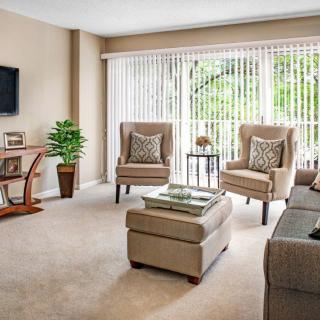 A cozy and well-lit living room featuring comfortable seating, a television, and large windows with blinds.