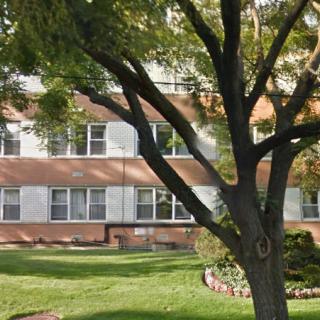 A large tree casting shadows on a lawn in front of a multistory building with several windows.