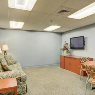 A cozy waiting room with a sofa, television, lamp, and decorative elements.