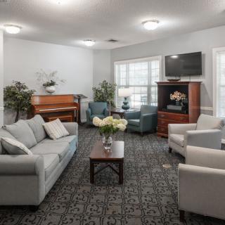 A cozy living room with sofas, armchairs, a piano, and a television.