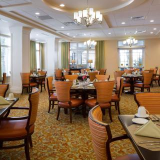 An elegantly decorated dining room with neatly arranged tables and chairs, illuminated by chandeliers.