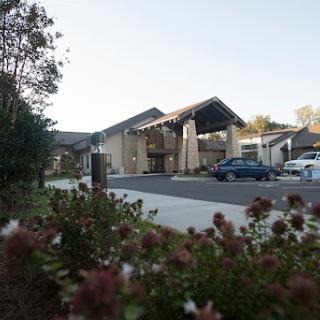 A modern architectural building surrounded by landscaped flowers and a parking area.