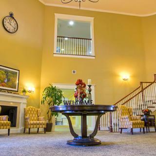 A spacious lobby with elegant decor, featuring a central round table and staircase.