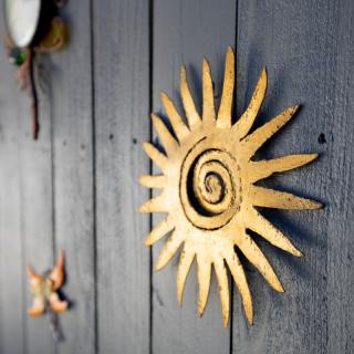A decorative metal sun with a spiral design mounted on a wooden wall.