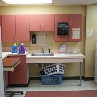 A laundry room with a sink, cabinets, and cleaning supplies.