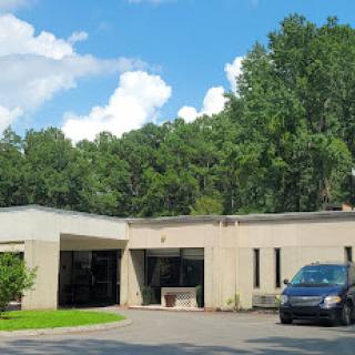 A modern building surrounded by greenery under a bright blue sky.