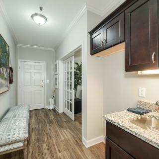 A well-lit hallway with wooden flooring, featuring a bench and cabinetry with a sink.