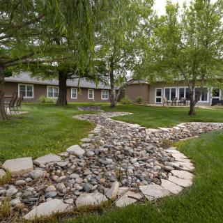 A tranquil garden with a winding rock path and lush greenery near a house.