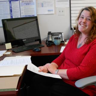 A woman smiling at her desk in an office setting.