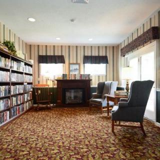 A cozy reading room with bookshelves, comfortable chairs, and a fireplace.