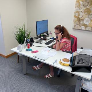 A woman engaged in a phone conversation at her office desk, surrounded by work materials and a snack.
