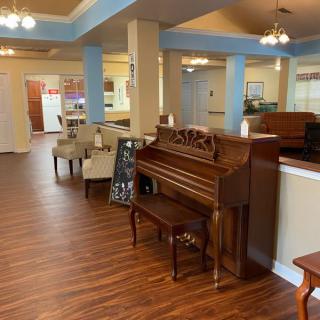 A spacious lounge area with a wooden floor features a piano, chairs, and cozy lighting.