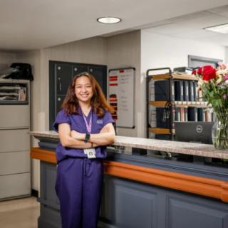 A nurse standing confidently at a hospital reception desk with flowers.
