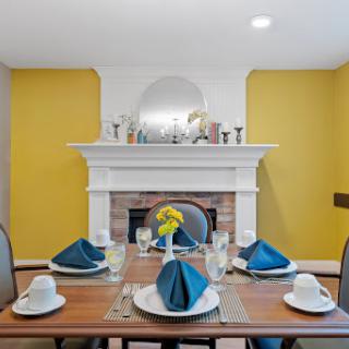 A beautifully designed dining room featuring a stylish table setting with blue napkins against a vibrant yellow wall and a classic fireplace.