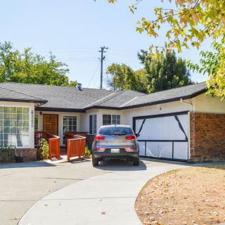 A suburban house with a car parked in the driveway and trees in the background.