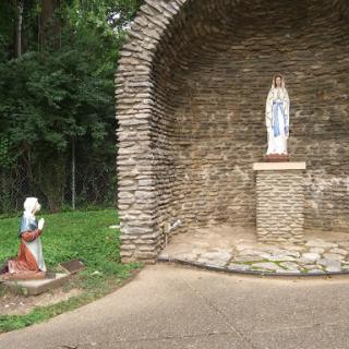 A serene outdoor shrine featuring a statue of a religious figure, accompanied by another statue in a prayerful pose.