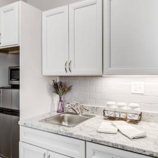 A modern kitchen with white cabinets and a marble countertop, featuring a sink and decorative elements.