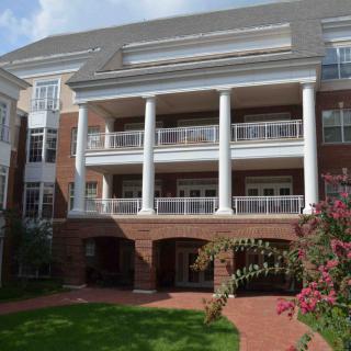 A large brick building with white columns and balconies surrounded by a garden.
