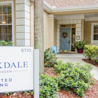 Entrance of a residential building with a sign, surrounded by greenery and well-maintained landscaping.