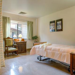 A serene hospital room featuring a bed, chairs, and natural light from the window.