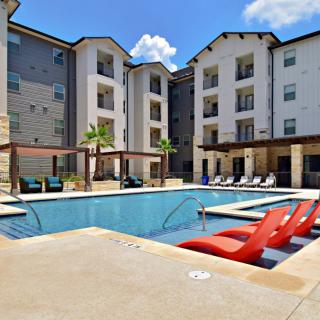 A modern apartment complex featuring a central swimming pool and outdoor seating area.