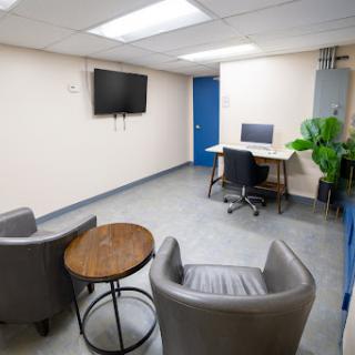 A modern office waiting area featuring comfortable seating, a computer station, and a television.