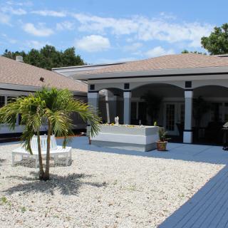 A spacious courtyard featuring a palm tree and outdoor seating, surrounded by a single-story house with archways.