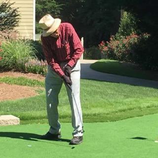 An elderly person putting on a golf green on a sunny day.
