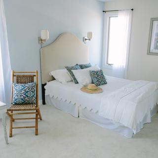 A bright and cozy bedroom with a neatly made bed, decorative pillows, and a wooden chair by the window.