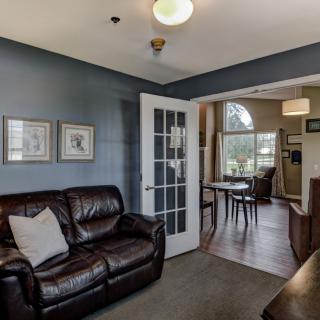 A cozy living room with a leather sofa and a view into the dining area through French doors.