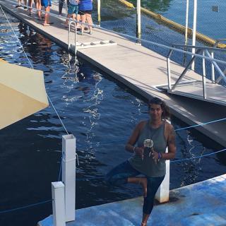 A person standing on a dock near the water, with a group of people in the background enjoying the day.