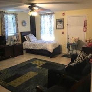 A cozy studio apartment with a combined bedroom and living area, featuring a bed, sofa, television, and decorative rug.