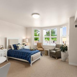 A cozy and well-lit bedroom featuring a bed, armchairs, and large windows bringing in natural light.
