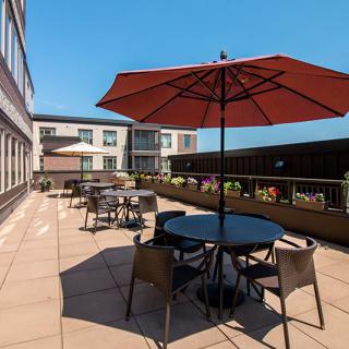 A sunny outdoor patio with tables, chairs, and umbrellas on a terrace next to a building.