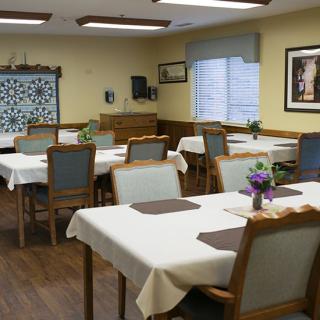 A cozy dining room with neatly set tables and comfortable chairs, illuminated by natural light through the windows.