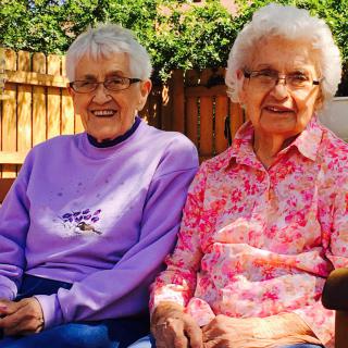 Two elderly women sitting and smiling in a garden.