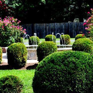 A landscaped garden featuring neatly trimmed hedges and a central fountain.