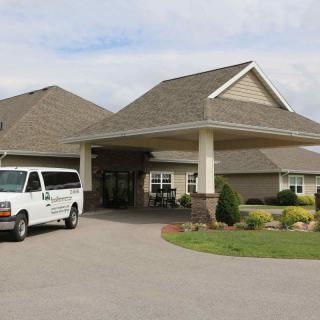 A building entrance with a parked van on the driveway and landscaped surroundings.