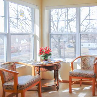 A cozy sitting area with two chairs and a table adorned with flowers, bathed in sunlight from large windows.