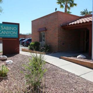 A brick building with a sign that reads 'Sabino Canyon' surrounded by desert landscaping under a clear blue sky.
