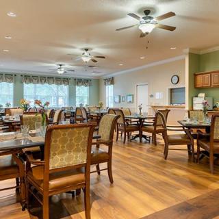 A well-lit dining area with wooden floors, tables, and chairs arranged neatly.