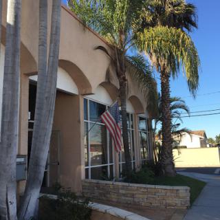 A view of a building adorned with palm trees and an American flag under a clear blue sky.