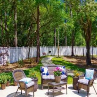 A tranquil backyard patio with seating surrounded by lush greenery and a white fence.