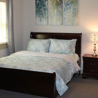 A cozy bedroom with a neatly made bed, nightstand and lamp, adorned with artwork above the headboard.