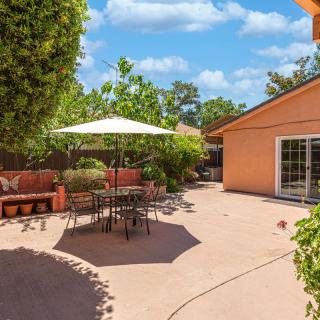 A spacious backyard patio featuring outdoor seating under a large umbrella, surrounded by lush greenery.