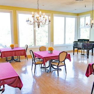 A bright and inviting dining area featuring tables set for guests, elegant chandeliers, and a piano for ambiance.